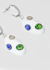 Par de aros colgantes con base de metal dorada, aro superior tipo argolla y dije ovalado de loza blanca con incrustaciones de piedras de colores: verde, azul y marrón.