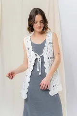 Chaleco tejido calado color crudo, con diseño artesanal, silueta relajada y largo a la cadera. Presenta terminación ondulada y detalle de lazo frontal.