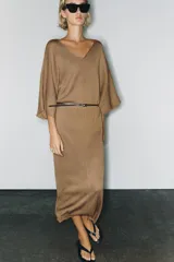 Vestido midi de punto color marrón con escote en V, mangas anchas y diseño holgado. Incluye un cinturón delgado marrón con hebilla metálica.