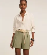 Short recto de cintura alta color verde oliva, confeccionado en viscolino, con trabillas en la cintura, pliegues y cierre tradicional. Incluye cinturón de rafia artificial con hebillas de argollas.