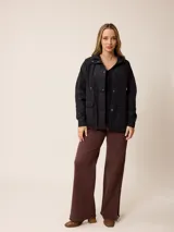 Campera de corte recto y estilo funcional, color beige, con capucha integrada, cierre frontal con botones a presión y bolsillos delanteros amplios. Presenta un diseño minimalista con cordones ajustables en la capucha.