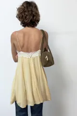 Vestido corto amarillo con escote en pico y tirantes finos ajustables. Presenta detalles de encaje blanco en el escote y en los laterales de la falda. Tiene forro interior y cierre en la espalda con cremallera y botones forrados.