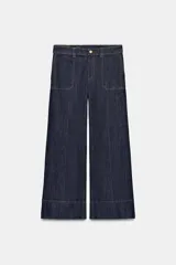Pantalón de jean tiro medio con corte culotte, pernera ancha y corta. Presenta bolsillos delanteros de plastrón, costuras decorativas verticales y cierre frontal con cremallera y botón.