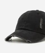 Gorra de sarga de algodón color negro con efecto desgastado y deshilachado en el borde de la visera y en la corona. Presenta dos argollas metálicas plateadas colgando del lateral de la visera.