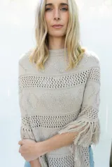 Poncho de tejido de algodón color beige claro, con diseño de punto calado y flecos en el borde inferior.