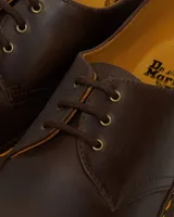 Zapato de tres ojales Dr. Martens modelo 1461, confeccionado en cuero Crazy Horse de color marrón con acabado encerado. Presenta costuras amarillas visibles en el borde de la suela y suela de goma con cámara de aire.