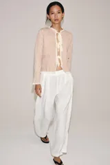 Chaqueta de punto color rosado con cuello redondo, manga larga y bolsillos delanteros. Presenta detalles de acabados con tejido combinado deshilachado en color blanco crudo y cierre frontal con lazos del mismo tono.