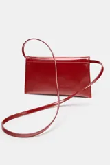 Bolso tipo bandolera de diseño estructurado, acabado brillante en color rojo y correa de cadena dorada. Cuenta con solapa frontal y doble compartimento interior.