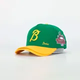 Gorra tipo baseball de color verde con visera amarilla. Presenta una letra B bordada en amarillo en el frente, la palabra Desires bordada en el lateral y un parche con diseño urbano y logo de la marca en el otro lateral.