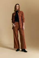 Pantalón de corte ancho y silueta relajada, confeccionado en tejido tipo gamuza color marrón. Presenta costuras verticales frontales que estilizan la pierna, cierre frontal con botón y bolsillos laterales.