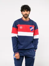 Buzo de cuello redondo confeccionado en felpa, con diseño de bloques de color en azul, rojo y blanco. Presenta el logo de Umbro y el escudo del Club Nacional de Football bordados en el frente.