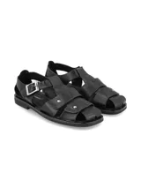 Sandalias de cuero color negro, de estilo romano con tiras cruzadas en el empeine, hebilla metálica de ajuste lateral y suela plana.