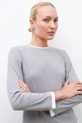 Remera gris melange de tejido canalé con cuello redondo y puños blancos, de manga larga.