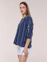 Blusa Erika de algodón con estampado de rayas en tonos azules, rosados y amarillos. Presenta cuello redondo con escote en V y botones frontales, mangas cortas decoradas con una fila de botones en los laterales y dobladillo asimétrico.