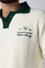 Sweater de punto con textura waffle en color blanco, con cuello polo en contraste color verde oscuro y cierre frontal de botones. Presenta un bordado decorativo en el pecho y un corte relajado.