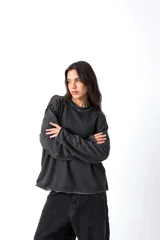 Buzo gris oscuro, estilo sweatshirt, con cuello redondo y terminaciones al corte en cuello, puños y cintura. Presenta un bordado en el frente.