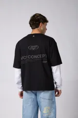 Remera de manga larga con diseño de doble capa, que combina una remera de manga corta color marrón moka con una base de manga larga blanca. Presenta un pequeño logo gráfico en el pecho y un detalle de etiqueta en el puño.