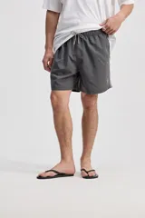 Short de baño oversize gris, con cintura elástica ajustable mediante cordón, bolsillos laterales y detalle de cinta estampada en los laterales.