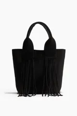 Bolso tipo shopper de color negro, confeccionado en tejido cepillado (similar a gamuza o nobuk). Presenta dos asas anchas con flecos largos colgantes en la parte frontal. Cierre magnético oculto en la parte superior y forro interior de tafeta con bolsillo con cierre.