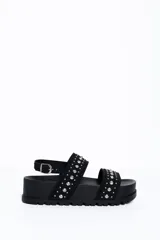 Sandalia chunky de plataforma color negro, con diseño de doble tira ancha decorada con tachas metálicas cónicas y pulsera ajustable al tobillo con hebilla.