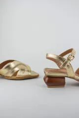 Sandalias doradas con capellada de cuero metalizado y malla, puntera cuadrada, tira ajustable al tobillo y taco geométrico de madera.