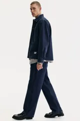 Pantalón tipo worker confeccionado en sarga de algodón de color azul marino, con un corte relaxed fit y piernas rectas. Presenta una cintura clásica con cierre de botón, bolsillos laterales al bies, bolsillos traseros, una trabilla funcional en un lateral y un bolsillo cargo dividido en el otro.