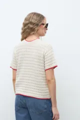 Remera de punto color crudo con detalles en rojo en el cuello y las mangas, manga corta y diseño texturizado.
