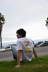 Remera blanca de algodón 100% peinado, de corte recto y manga corta, con estampa en la espalda de bananas con intervenciones de color y texto.