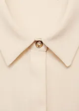 Vestido midi de tejido fluido en color beige, con cuello camisero, cierre frontal de botones y mangas cortas con vuelta. Presenta un diseño entallado con detalles drapeados en el lateral de la cintura.