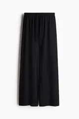 Pantalón negro de tiro alto, confeccionado en tejido texturizado con corte holgado y piernas amplias. Cuenta con cintura elástica fruncida y cordón ajustable.