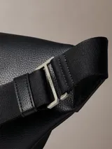 Riñonera Calvin Klein de poliuretano texturizado color negro, con cierre superior de cremallera y un bolsillo frontal con cierre. Cuenta con correa ajustable y detalles metálicos plateados.