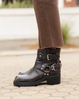 Botas de cuero estilo biker en color marrón oscuro con efecto desgastado. Presentan un diseño de caña corta con correas ajustables con hebillas metálicas y detalles de remaches. Cuentan con una suela de goma dentada y tacón bajo.