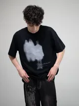 Remera negra de algodón con estampado frontal en blanco que simula dos figuras borrosas y una firma manuscrita con el texto "bullet hole" debajo.