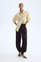 Pantalón de sarga de tiro alto color marrón oscuro, con bolsillos laterales discretos, pinzas y diseño de piernas globo con puños abotonados con frunces.