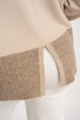 Sweater tipo polera de calce oversize, con diseño color block que combina tonos beige y marrón. Presenta cuello alto, mangas largas con puños acanalados y un panel inferior acanalado a juego.