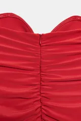 Vestido largo de fiesta color rojo, con escote corazón y diseño palabra de honor. Presenta detalles de drapeado lateral y una superposición de tela con lazada en la cintura, con falda de corte evasé.