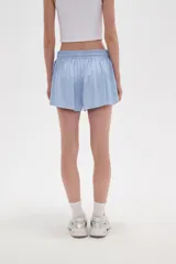 Short de poliéster color celeste, de calce holgado y tiro alto, con cintura elástica ajustable mediante cordón y bolsillos laterales.