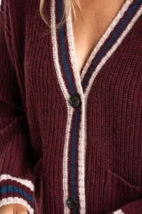 Cardigan de punto color bordó con diseño oversize, cuello en V y cierre frontal con botones. Presenta detalles de rayas en contraste en color crema y azul en los bordes, puños y ruedo, además de dos bolsillos frontales aplicados.