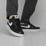 Championes Nike Court Vision Low Next Nature, de estilo urbano inspirado en el básquet de los años 80. Presentan un diseño de corte bajo con capellada de cuero sintético en color negro, destacando el icónico logo de la marca en blanco en los laterales. Cuentan con perforaciones en la puntera para mayor ventilación, cuello acolchado y suela de goma blanca vulcanizada que brinda tracción y durabilidad.