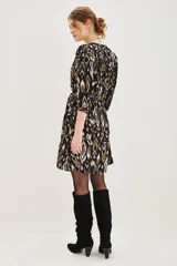 Vestido corto de corte recto con estampado ikat en tonos negro, blanco y ocre. Presenta escote en V con cierre de botones, mangas tres cuartos con puños elásticos y un cinturón de la misma tela para ajustar la cintura.