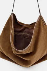 Bolso tipo shopper de textura acanalada efecto pana, color marrón. Cuenta con asa de hombro, cierre frontal con tira y hebilla metálica, y bolsillo interior con cremallera.