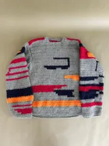 Buzo de lana gris tejido a crochet con cuello redondo y mangas largas. Presenta detalles geométricos en rojo, naranja y azul marino.