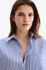 Camisa corta oversize de popelina de algodón con rayas verticales blancas y azules, cuello clásico, cierre frontal de botones, bolsillo en el pecho y mangas tres cuartos con puños anchos.