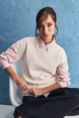 Chaleco de tejido de punto color beige claro, con cuello redondo y diseño de líneas limpias con hombros caídos y terminaciones acanaladas.