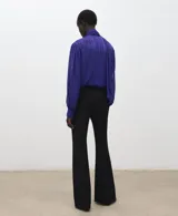 Blusa de poliéster color azul, con cuello alto, lazada integrada, cierre lateral con botones y mangas largas abullonadas con puños ajustados.