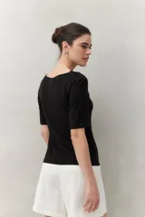 Remera blanca de manga corta con escote asimétrico y detalle de nudo con frunces en el centro del busto.