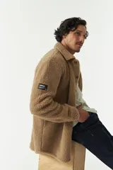 Sobrecamisa de sherpa color crema con cuello camisero, cierre frontal con botones a presión y bolsillo de parche en el pecho. El modelo usa talle M.