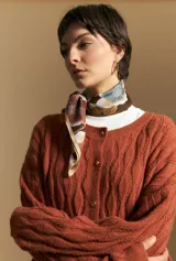 Cardigan de punto color terracota con diseño de trenzas verticales, cuello redondo y cierre frontal con botones metálicos. Presenta mangas largas con puños ajustados y un calce holgado.