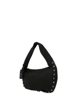 Cartera hobo de cuero sintético negro de la marca Hush Puppies, modelo Taffy. Presenta un diseño suave con una correa ancha para el hombro y detalles de tachas metálicas redondas a lo largo de los bordes laterales e inferiores. Incluye un llavero colgante con la silueta del perro basset hound característico de la marca y el logo impreso en la parte frontal.