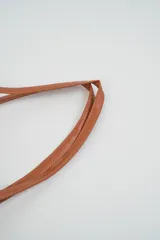 Bolso tipo tote bag de rafia tejida color beige, con asas y solapa superior de cuero marrón. Incluye un colgante decorativo con borlas de cuero.